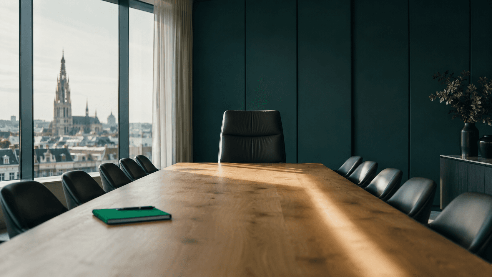 An empty boardroom chair at the head of an oak table, Antwerp rooftops through the window